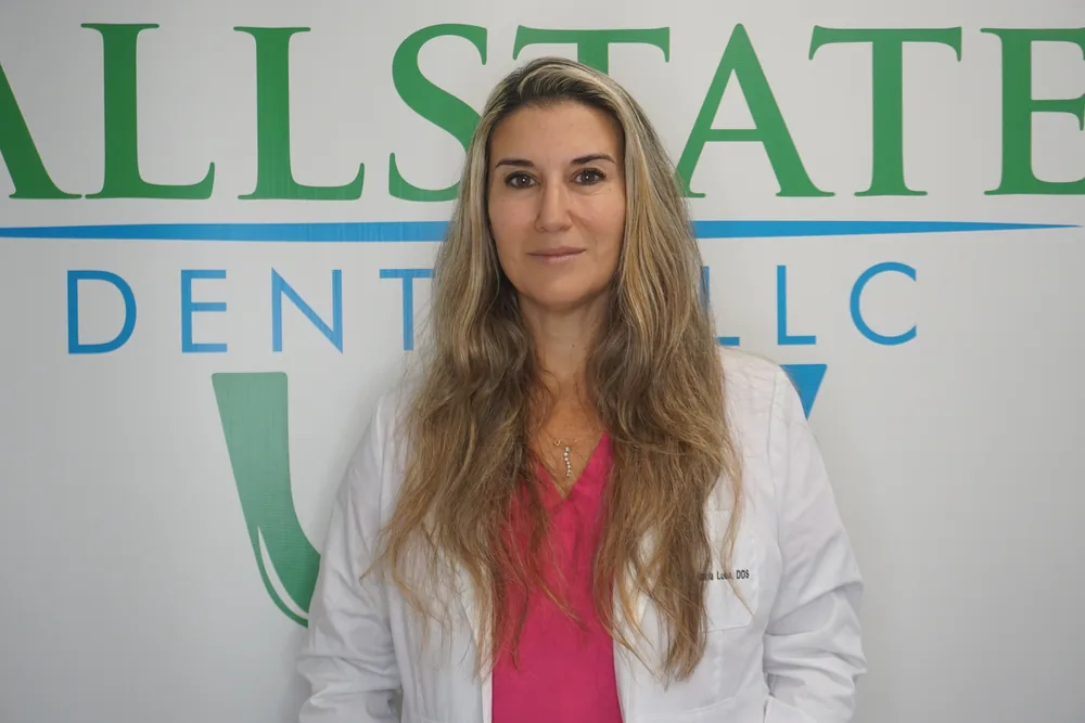 Dr. Maria Luba of Allstate Dental in front of the office logo